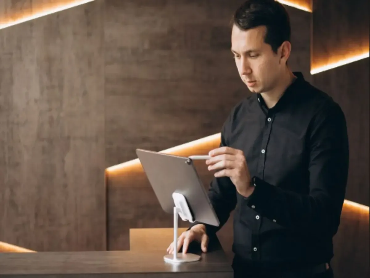 Hotel staff member using a touchscreen point-of-sale system to manage guest orders and service requests at a hospitality reception desk.