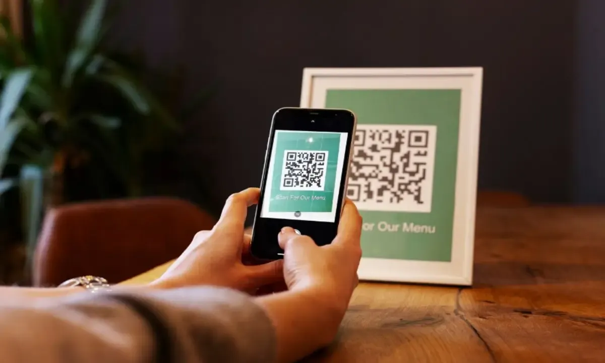 Customer using smartphone to scan QR code menu at hotel restaurant table for quick contactless ordering and digital dining experience.